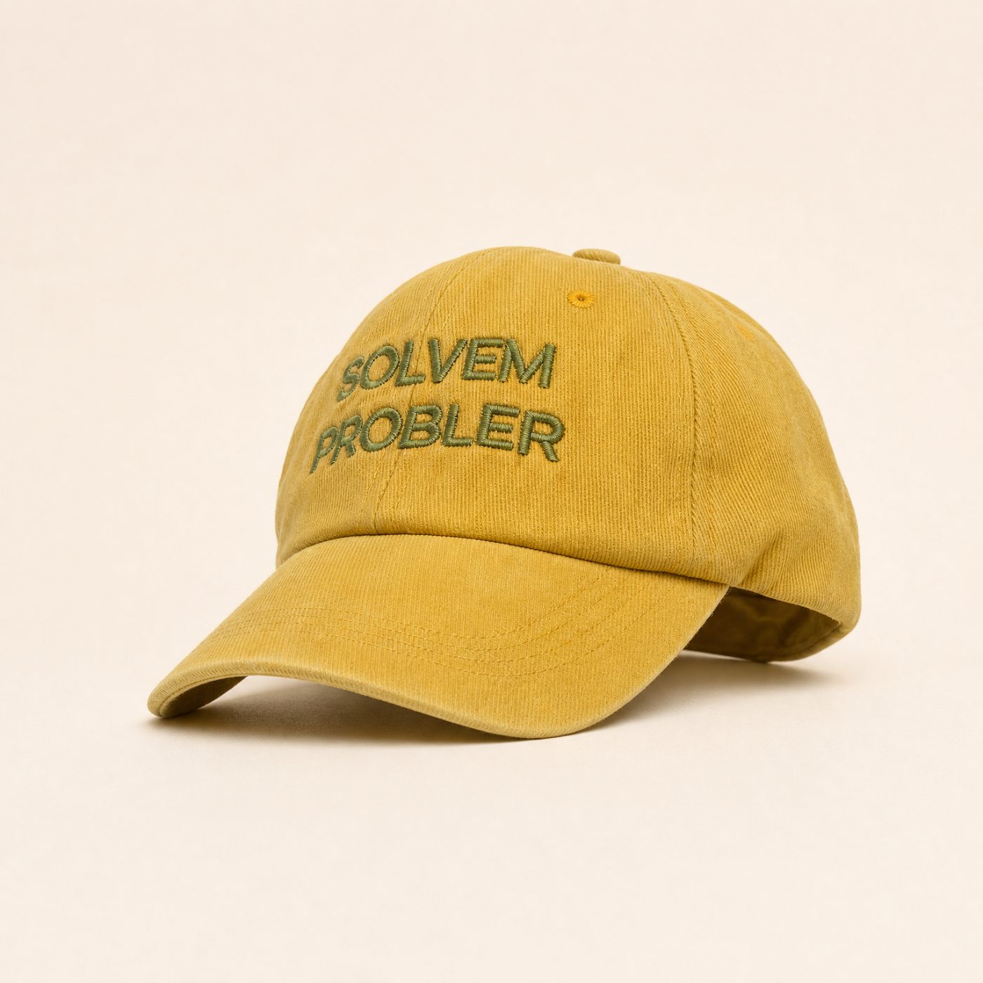 Mustard yellow baseball cap with embroidered text 'SOLVEM PROBLER' on a checkered fabric hat stand on a wooden table