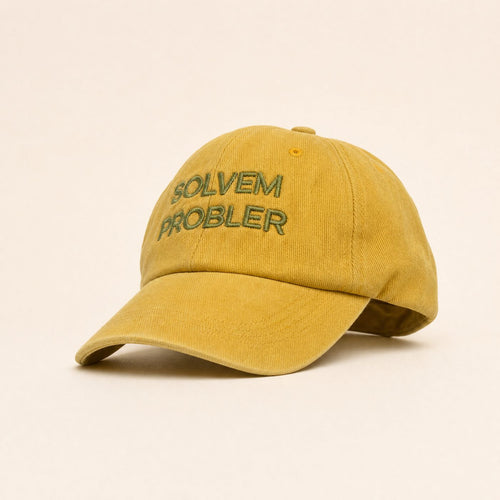 Mustard yellow baseball cap with embroidered text 'SOLVEM PROBLER' on a checkered fabric hat stand on a wooden table