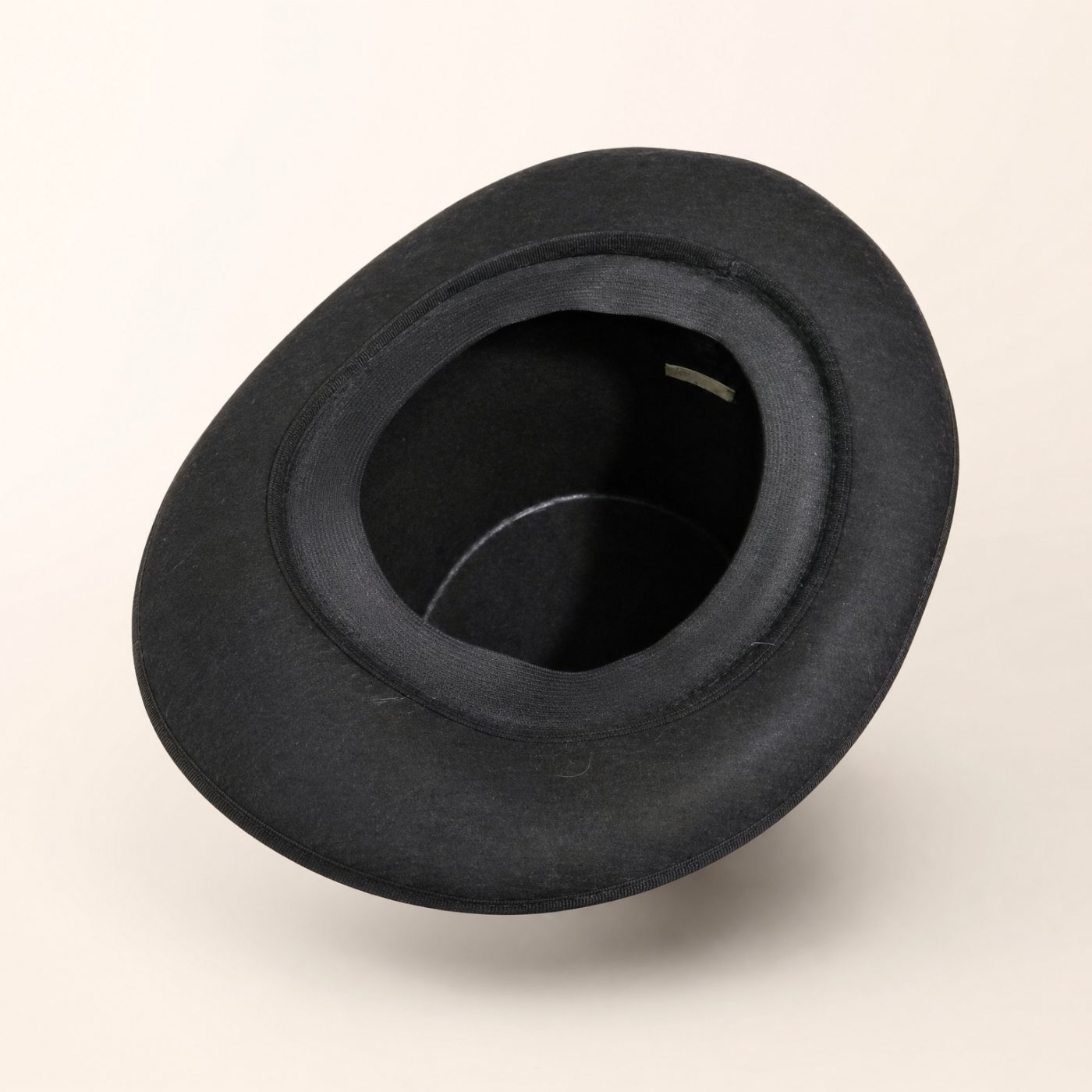 Black felt top hat with a tall cylindrical crown and narrow curved brim placed on a cushioned chair